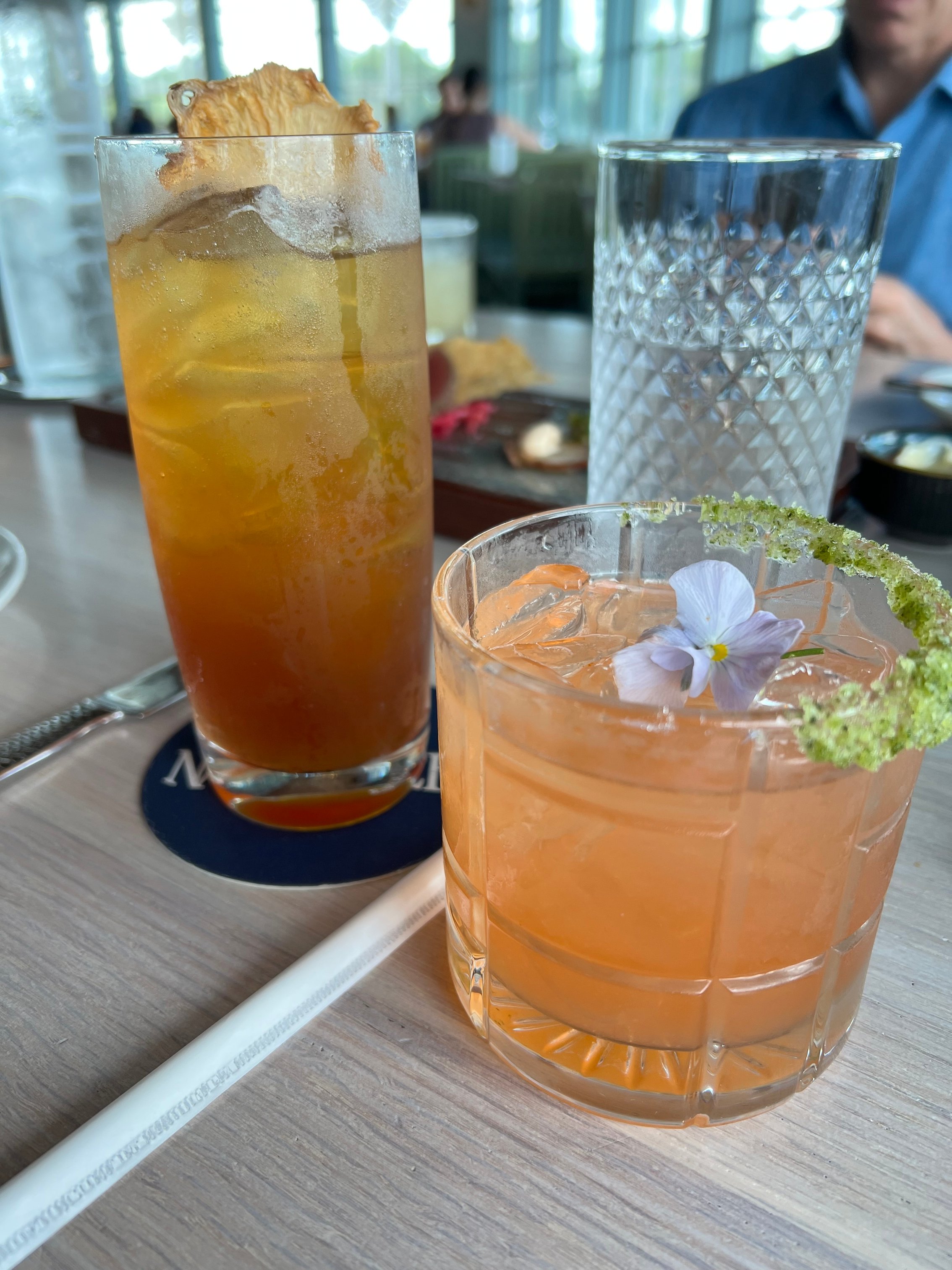 Two cocktails with floral garnishes and a glass of water