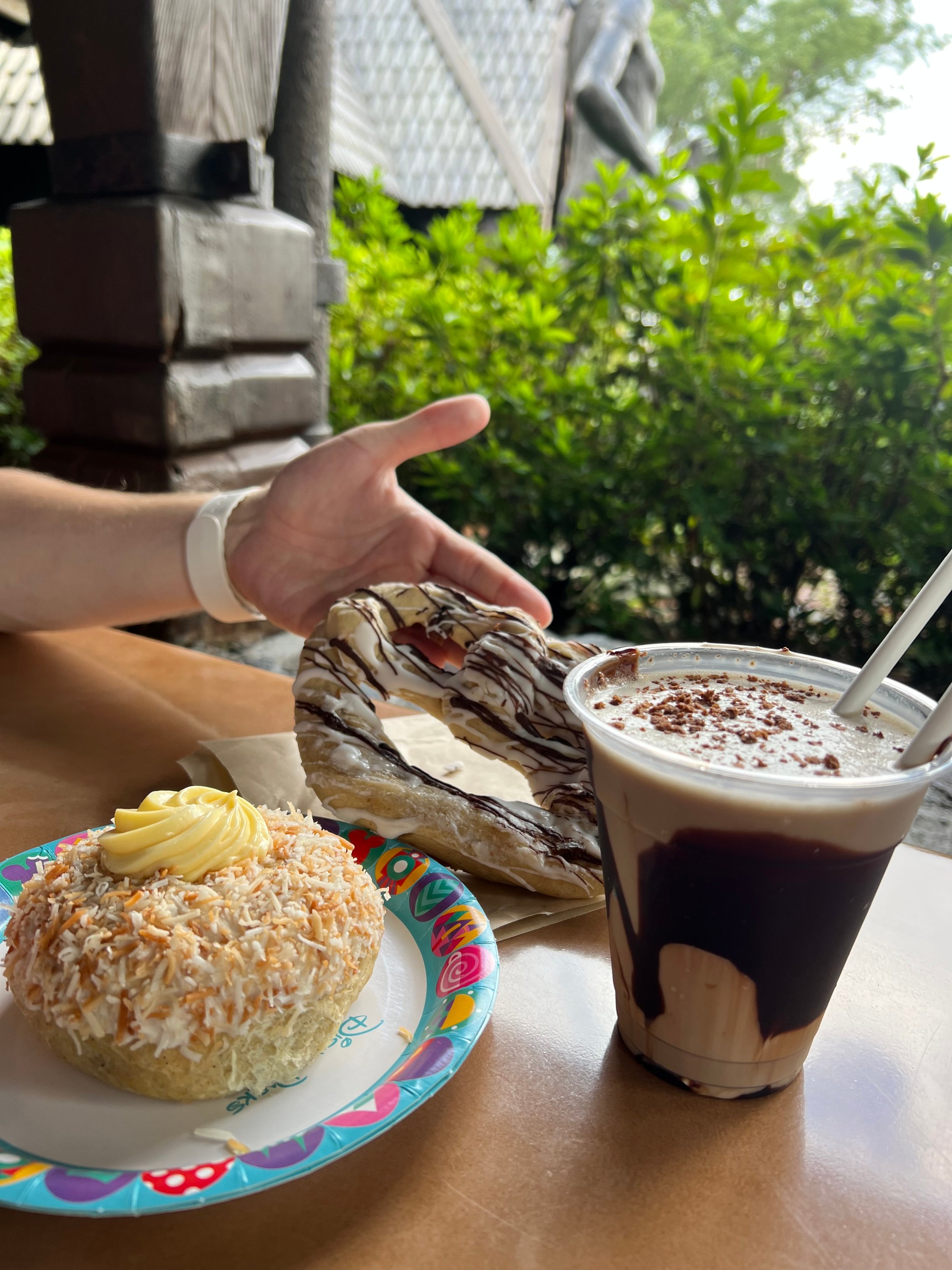 A large cupcake with sprinkles, a pastry, and a chocolate frozen drink on a table